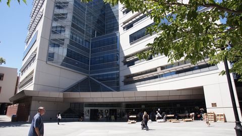 People walking past the glass entrance of the Dr. Martin Luther King Jr. Library in Downtown San Jose, home to several free library book clubs