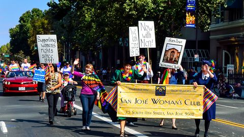 Marchers carrying signs and a banner down a tree-lined Downtown San Jose street during the Silicon Valley Pride Parade