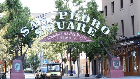 The arched San Pedro Square sign over a tree-lined street in Downtown San Jose, with a banner for the Friday farmers market