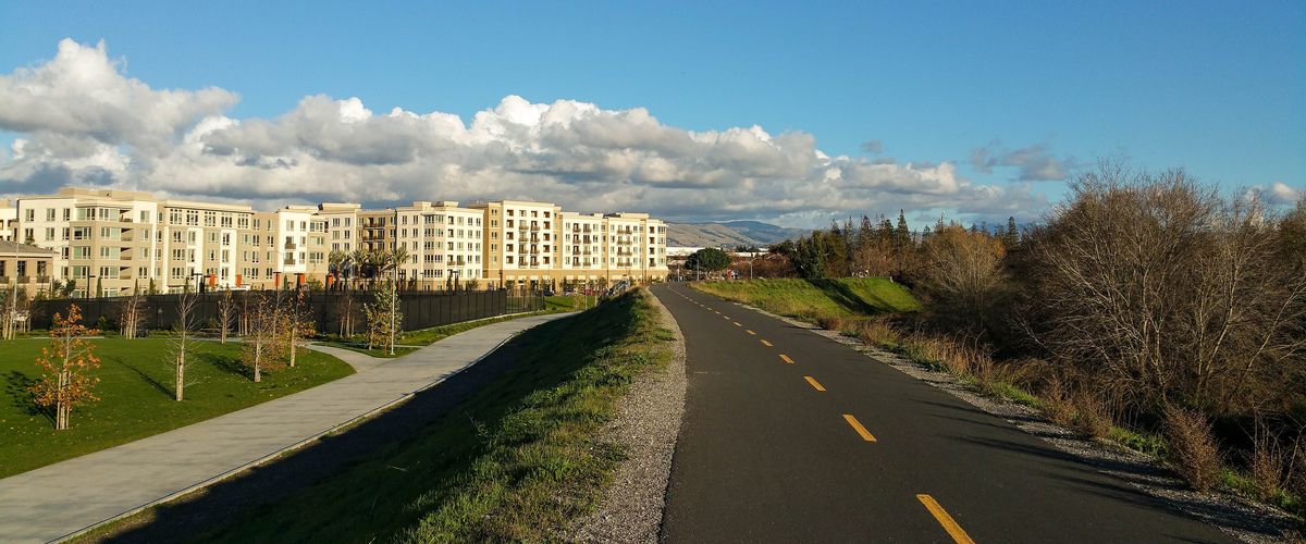 Paved Guadalupe River Trail in San Jose curving past grass and trees under a blue sky, a common route for group runs